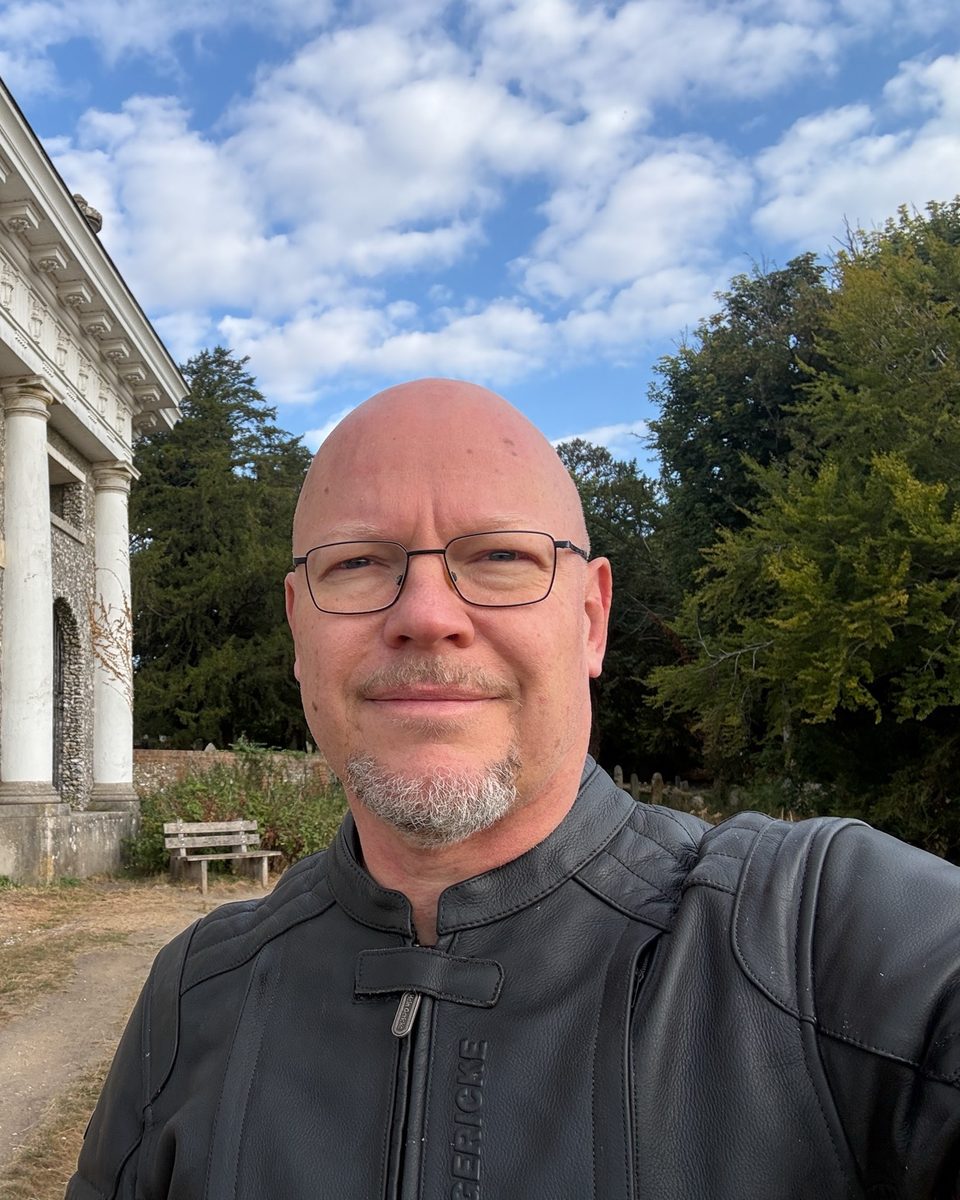 Andy Greening in his motorcycle jacket, in front of a flint-and-stone folly with white columns