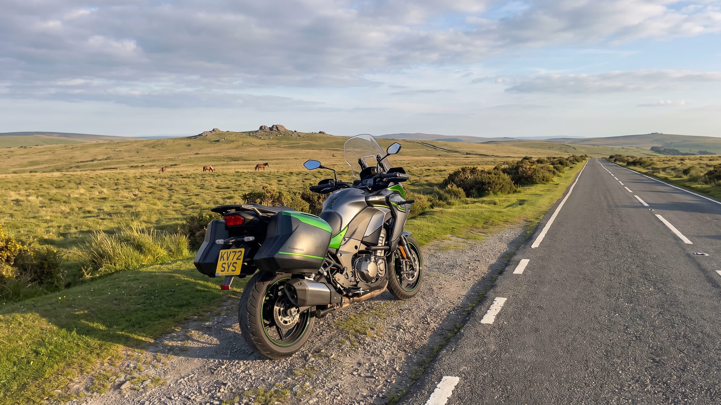 A motorcycle beside an open moorland road with a granite tor and grazing ponies