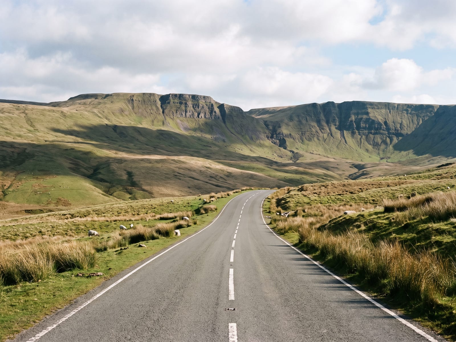 Near Brecon: a wide two-lane road crossing open green-brown moorland beneath steep escarpments in the Brecon Beacons, Wales