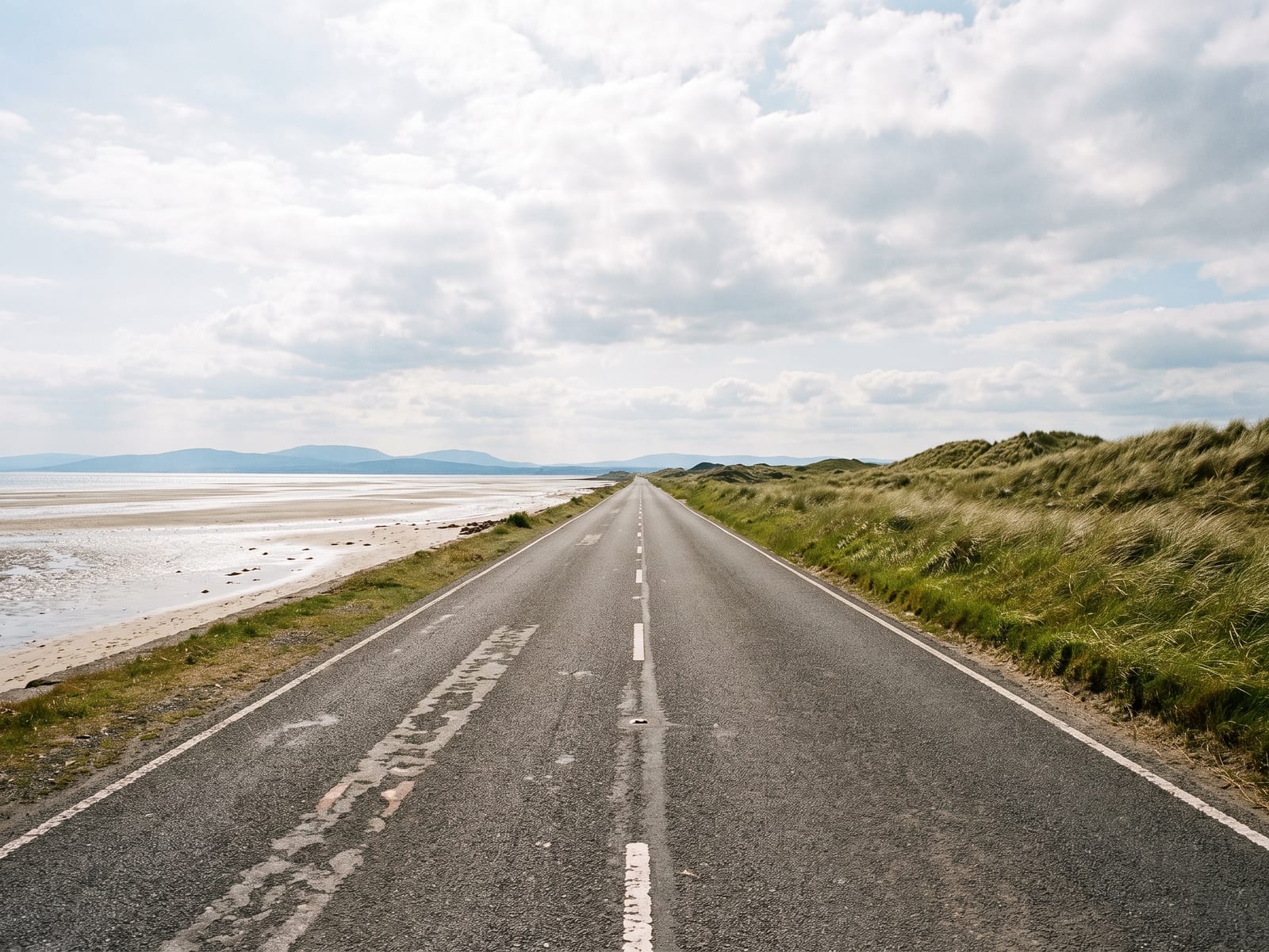 Near Cockermouth: a flat, straight two-lane coast road running beside a pale tidal shoreline on the north-west coast of Cumbria