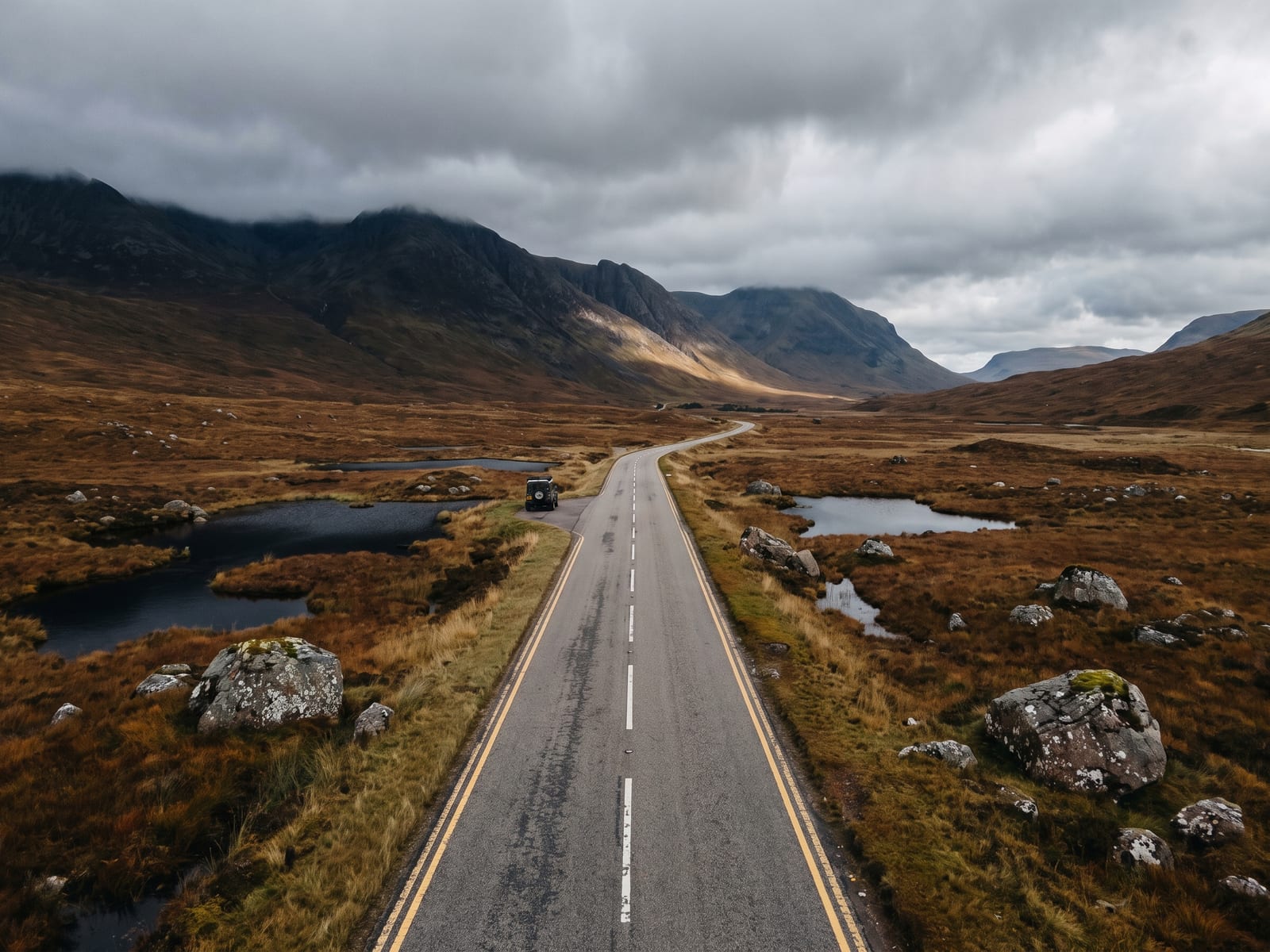 Near Fort William: a broad tarmac road crossing a vast treeless Highland moorland basin with steep dark mountains on the horizon, Scotland, rust-brown grasses