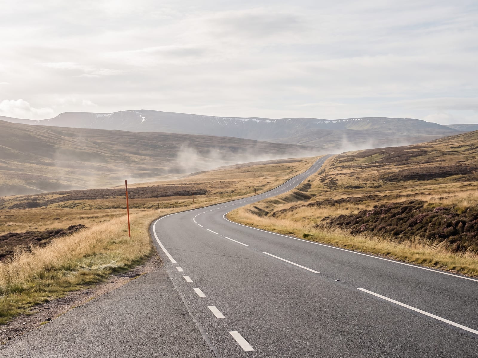 Near Grantown-on-Spey: a smooth tarmac road crossing a high rolling Highland moor in the eastern Cairngorms, Scotland, faded gold grass and dark heather