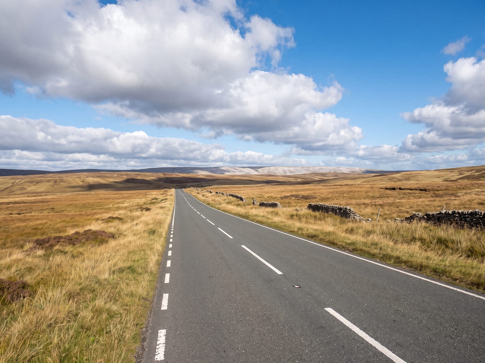 Near Hexham: a long road crossing a high open moor with tawny grass and a few stone walls in Northumberland, a pale ridge on the horizon