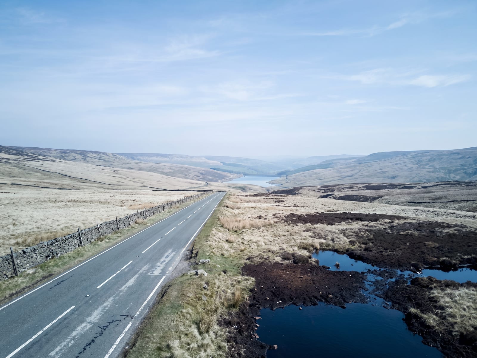 Near Holmfirth: a tarmac road crossing a high Pennine moor above a narrow valley with a pale reservoir far below
