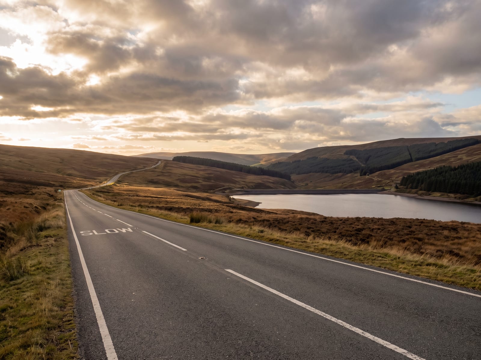 Near Machynlleth: a smooth two-lane road climbing across a wide open mountain moor above a still reservoir in the Cambrian Mountains, Wales
