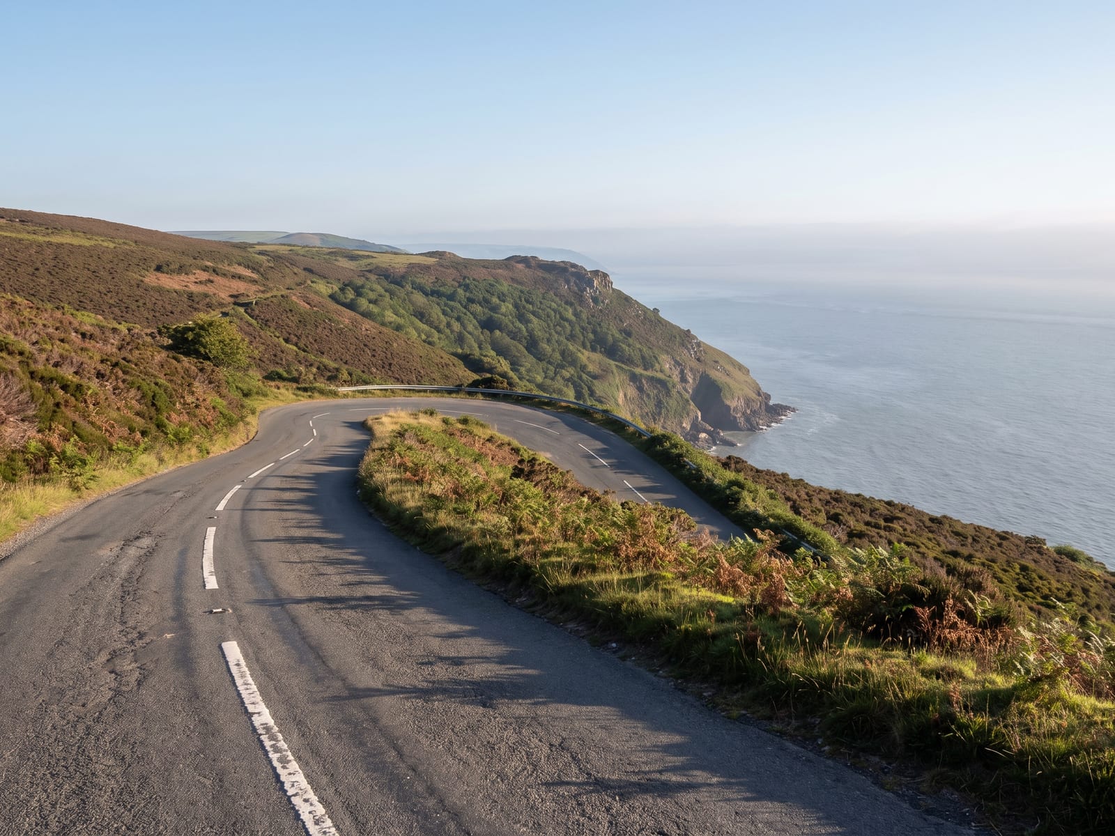 Near Minehead: a winding coastal road with a hairpin bend high above a rugged wooded cliff-line and a wide grey-blue sea in Exmoor, Somerset