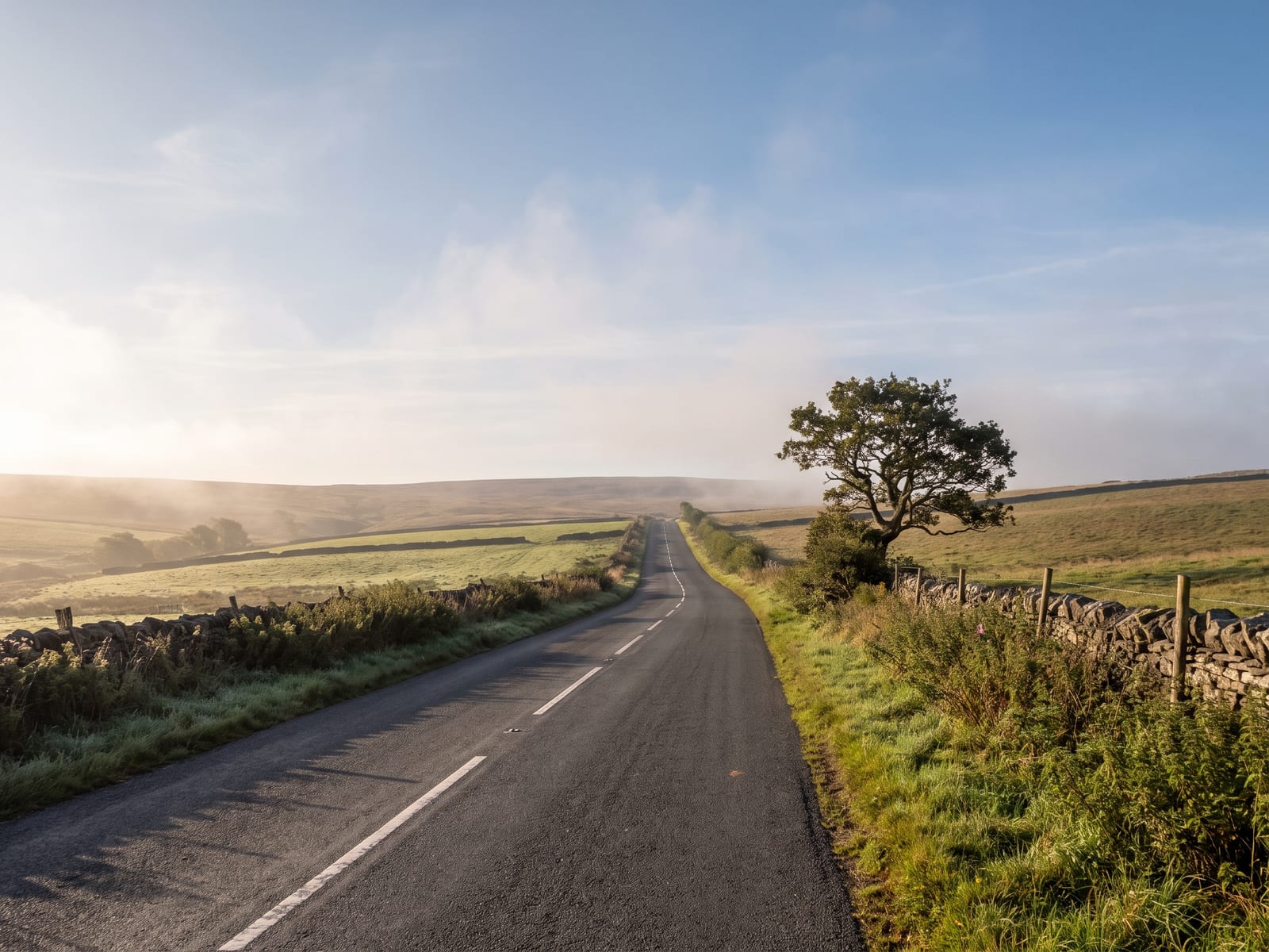 Near Okehampton: a narrow two-lane country road crossing high farmland towards a distant open moor in Devon, hedgerows