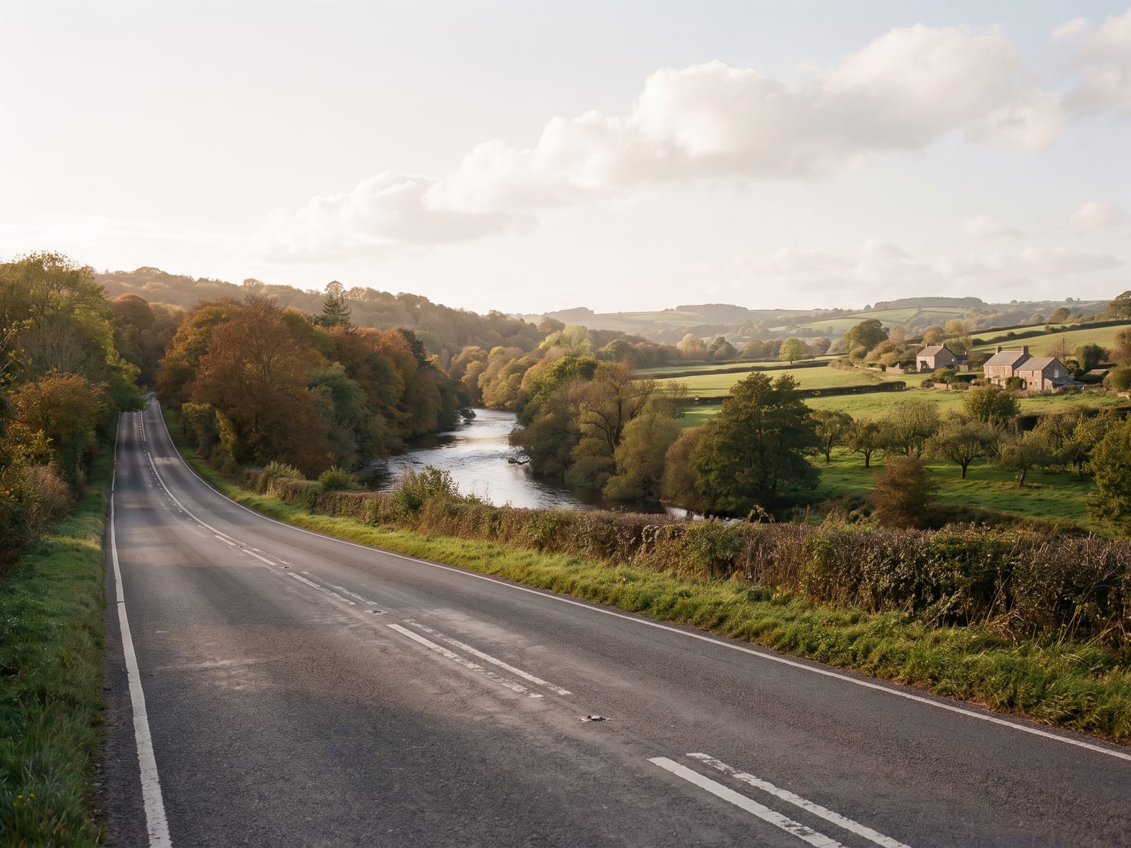 Near Okehampton: a wide two-lane road running beside a wooded river valley with patchwork fields and orchards in Devon