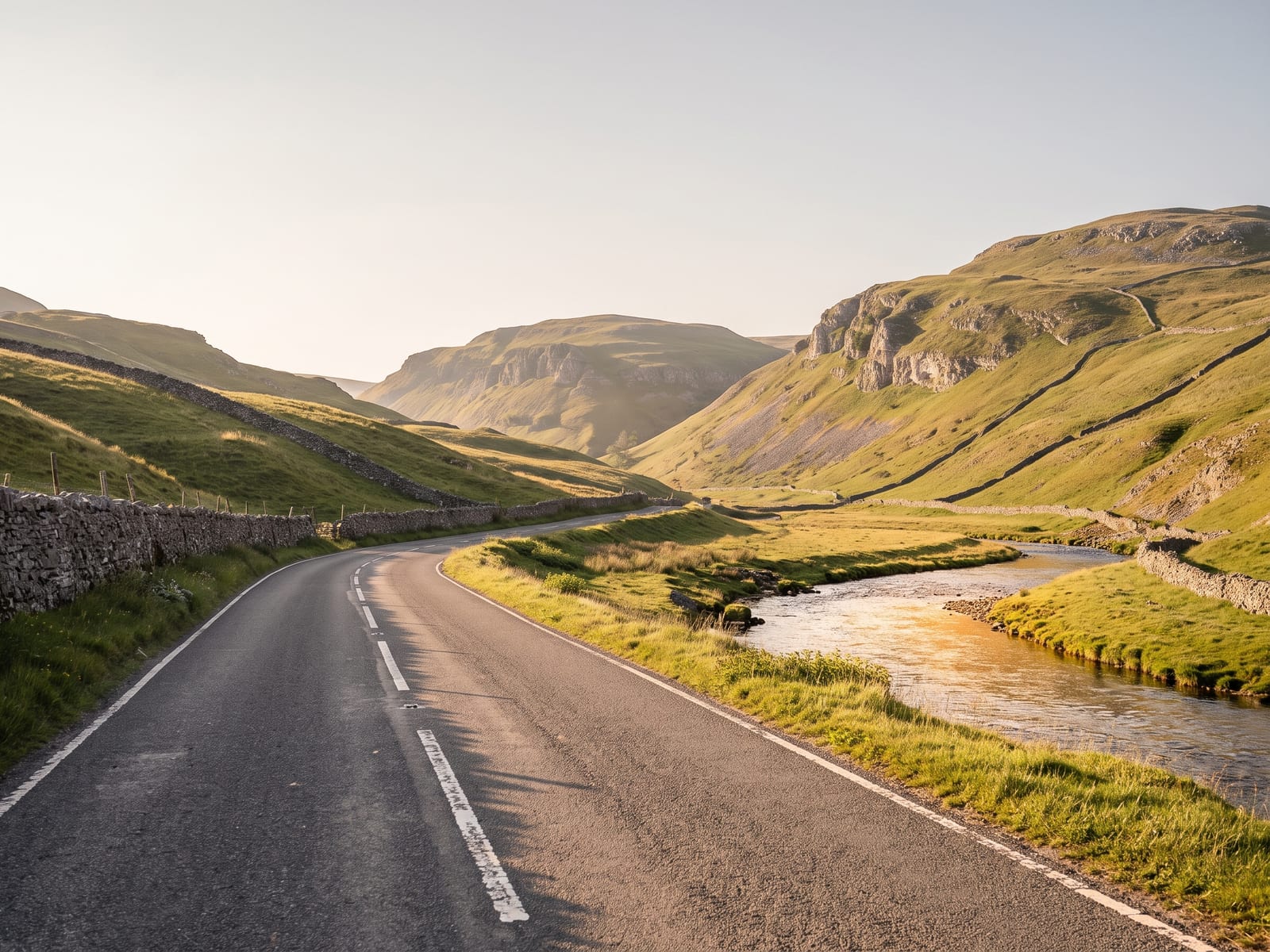 Near Settle: a tarmac road running through a limestone dale in the Yorkshire Dales, steep grey scars and rounded hills beyond